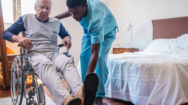 Male in a wheelchair with male care assistant helping him.