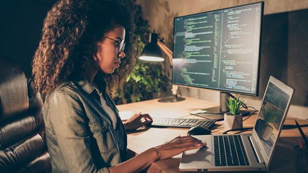 Woman coding on laptop and second screen