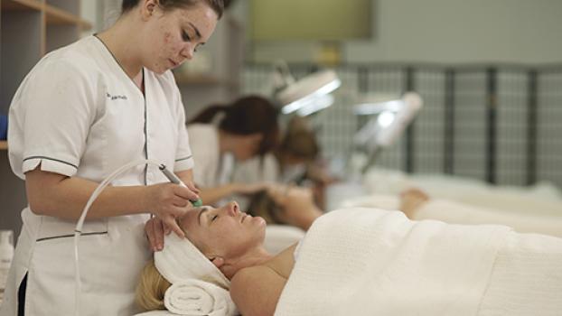 Female beauty technician performing facial treatment on female client.