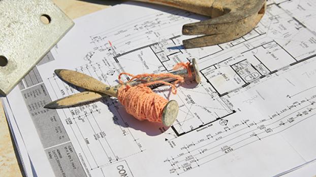 Image of building plans with hammer and pegs and string.