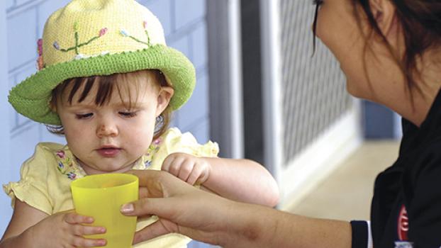 Young toddler being handed a cup by a childcare worker.