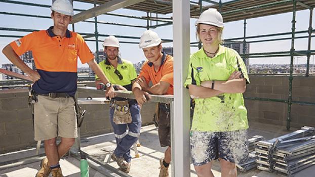 Group of tradespersons stood with scaffolding surrounding them.