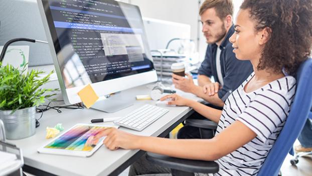 Young woman and young man at a desk in front of a machine with website code