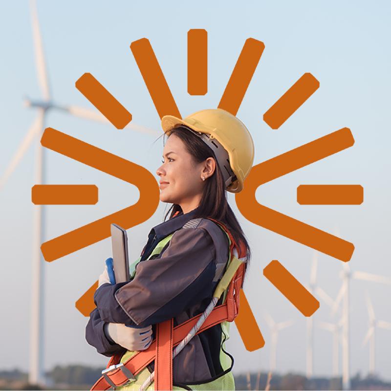 A woman in high-visibility workwear, standing in front of a wind turbine.