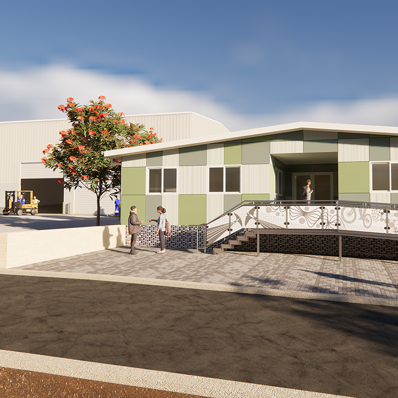 A modern green‑and‑white building with an accessibility ramp in front, with people walking nearby and industrial sheds and forklifts in the background on a sunny day.