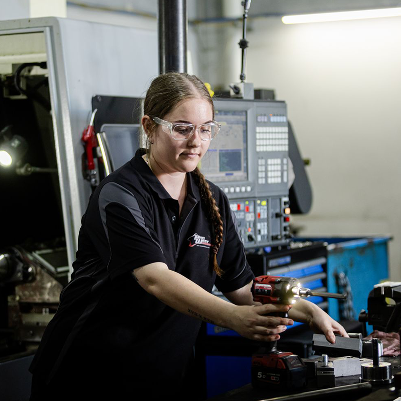 Person using a power drill while working with metal parts in a machining workshop.