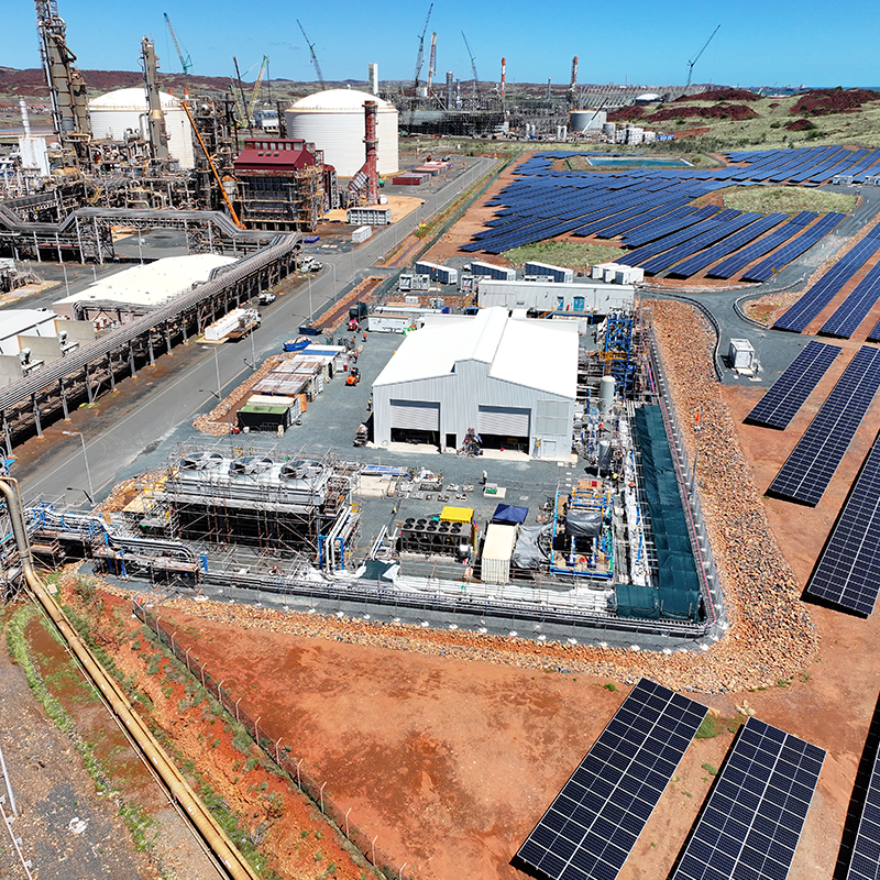 Aerial view of an industrial site with storage tanks, processing structures, and nearby solar panels. 