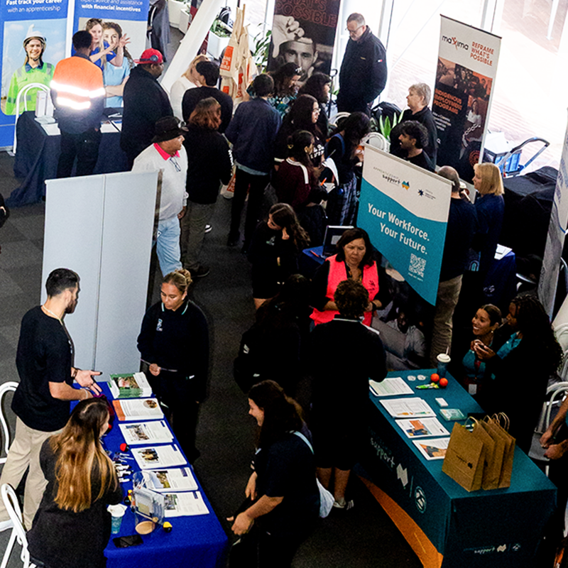 Busy Deadly Jobs Expo with attendees visiting exhibition booths, speaking with representatives, and browsing training and employment information. 