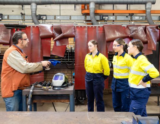 TAFE lecturer and heavy fabrication students standing in workshop.