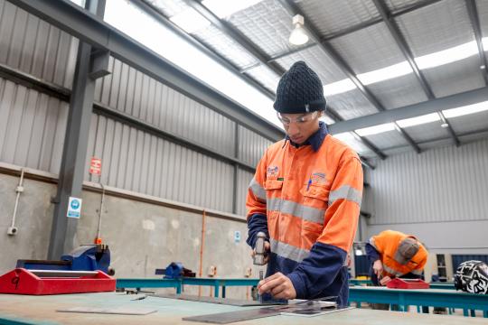 TAFE student using hammer and nails on table.