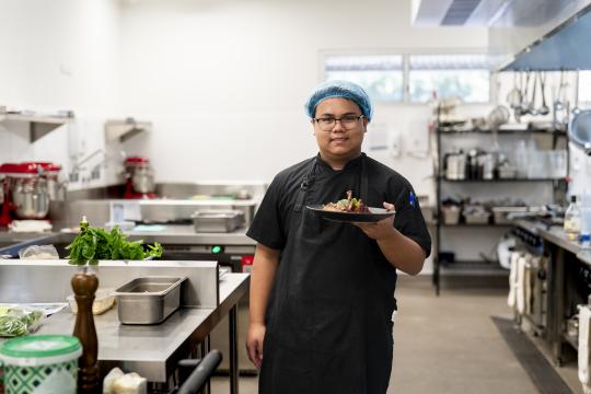 Chef student holding plate of food in kitchen.