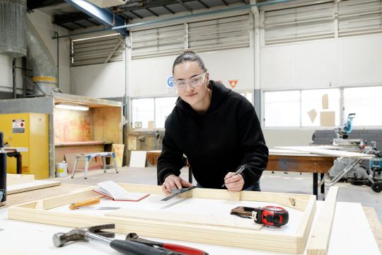 Female carpenter measuring wood on table with ruler.