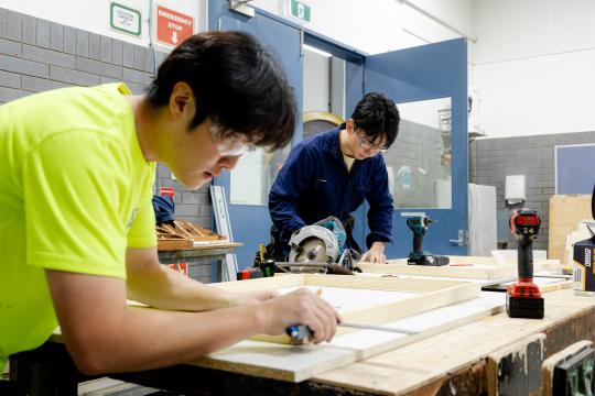 Two TAFE students measuring wooden frames.