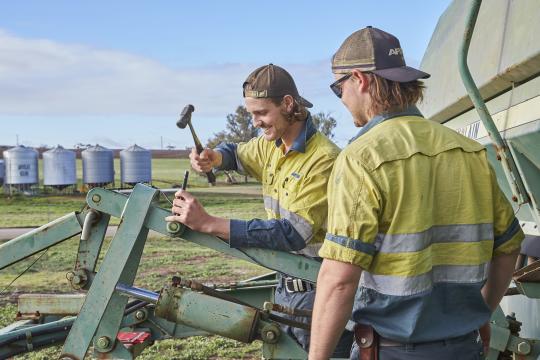 Two heavy diesel mechanic students fixing part of farming equipment.
