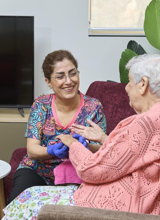 Community services student helping elderly client with painting nails.