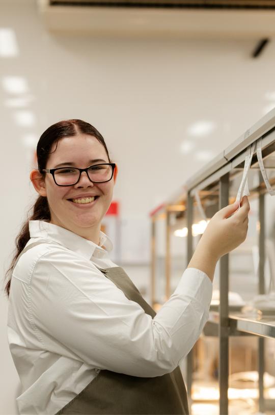 Hospitality student smiling while holding order ticket in kitchen.