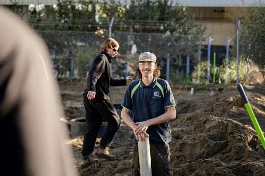 Plumbing student outdoors placing pipes in ground.