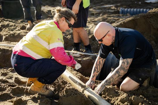 Plumbing students outdoors placing pipes in ground.